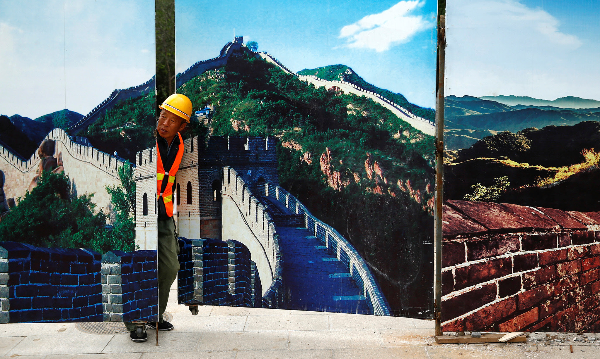 A worker looks through the fence of a construction site that is decorated with pictures of the Great Wall at Badaling, north of Beijing, China, September