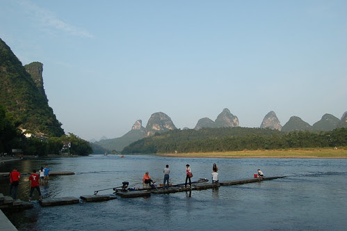 Vor einer Kette vom Karstbergen im Hintergrund ist der Yulong Fluss. Im Vordergrund steigen gerade Passagiere von den Bambussflössen.