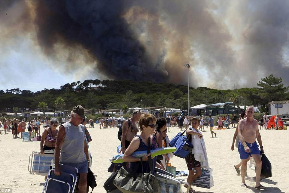 On the move: Sunbathers were evacuated after heading to the beach this morning in Le Lavandou. They were seen carrying their beach chairs away as black smoke rose up from a fire on a nearby hill