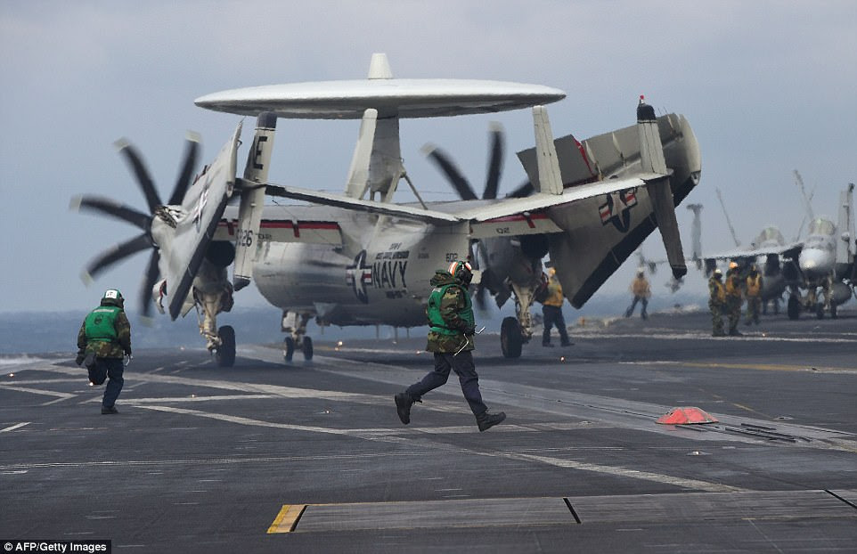 US Navy crew members run next to an E-2C Hawkeye as it lands on the deck of the USS Carl Vinson