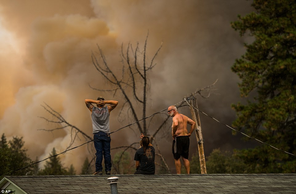 Home owners Daniel Ravera, left, and Bill Stafford, right, stand on a neighbor's home to watch the fire move towards their property Sunday