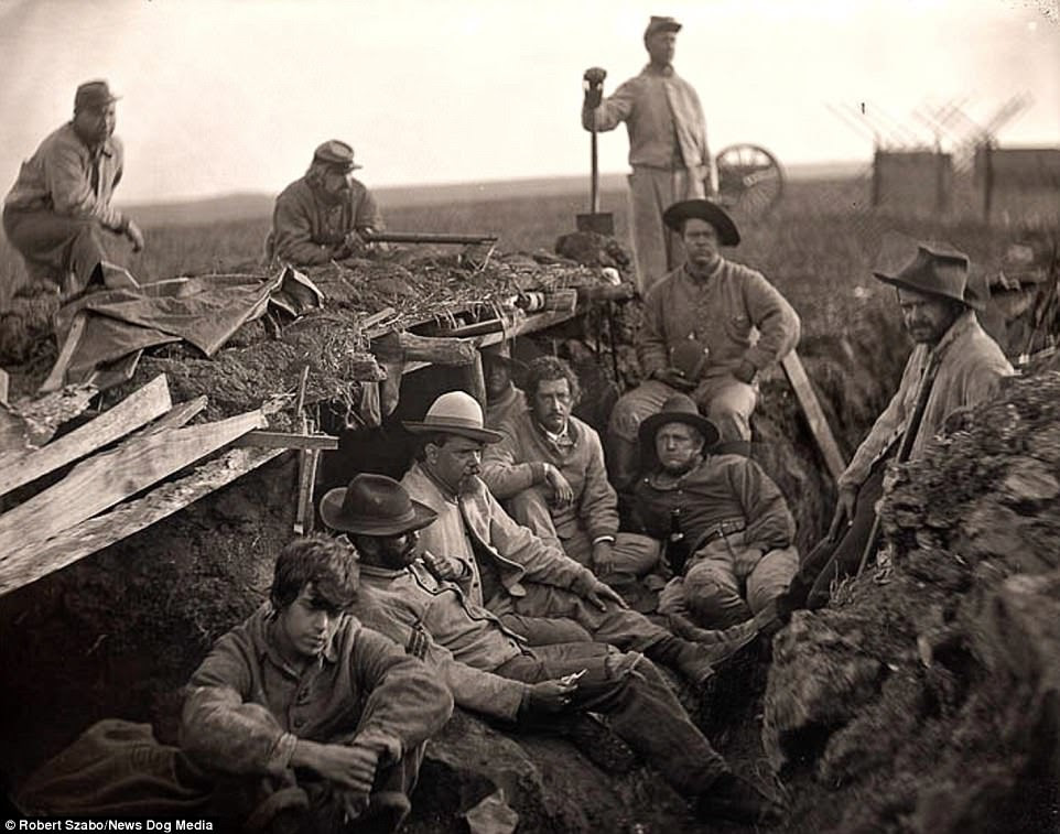 This photo taken by Robert Szabos shows a group of men lying in a trench. One is pointing a gun on top of the trench while another stands with a shovel