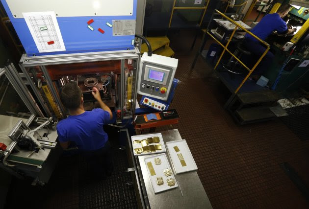 An employee places a gold Combibar into a press machine at a plant of gold refiner and bar manufacturer Valcambi SA in the southern Swiss town of Balerna