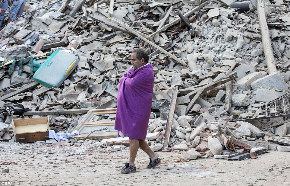 Um homem coberto em um cobertor anda na frente dos escombros parece andar em sapatos de criança depois de escapar do terremoto