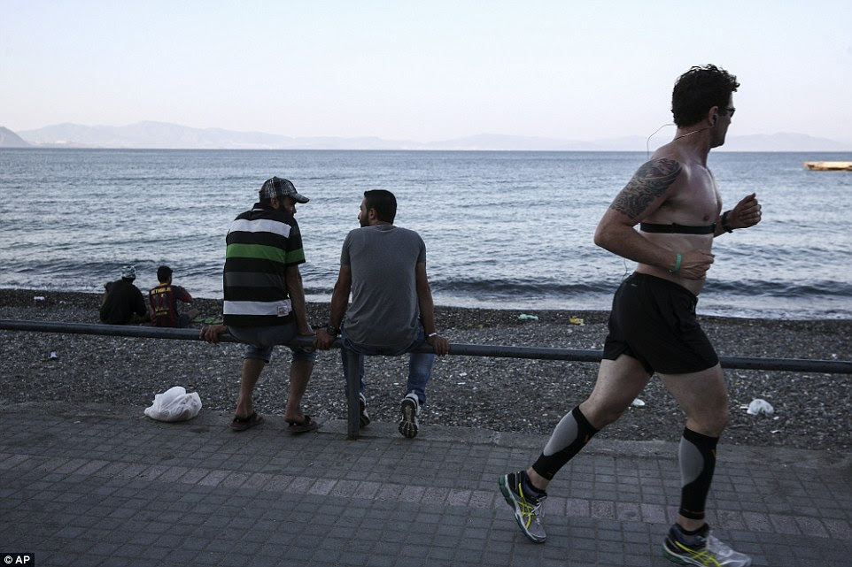Going for a run: A tourist jogs along a promenade past migrants overlooking a beach at Kos town yesterday evening