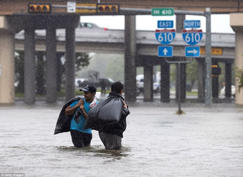 Two men carry their belongings across a flooded road after fleeing their apartment in North Braeswood Boulevard on Monday 