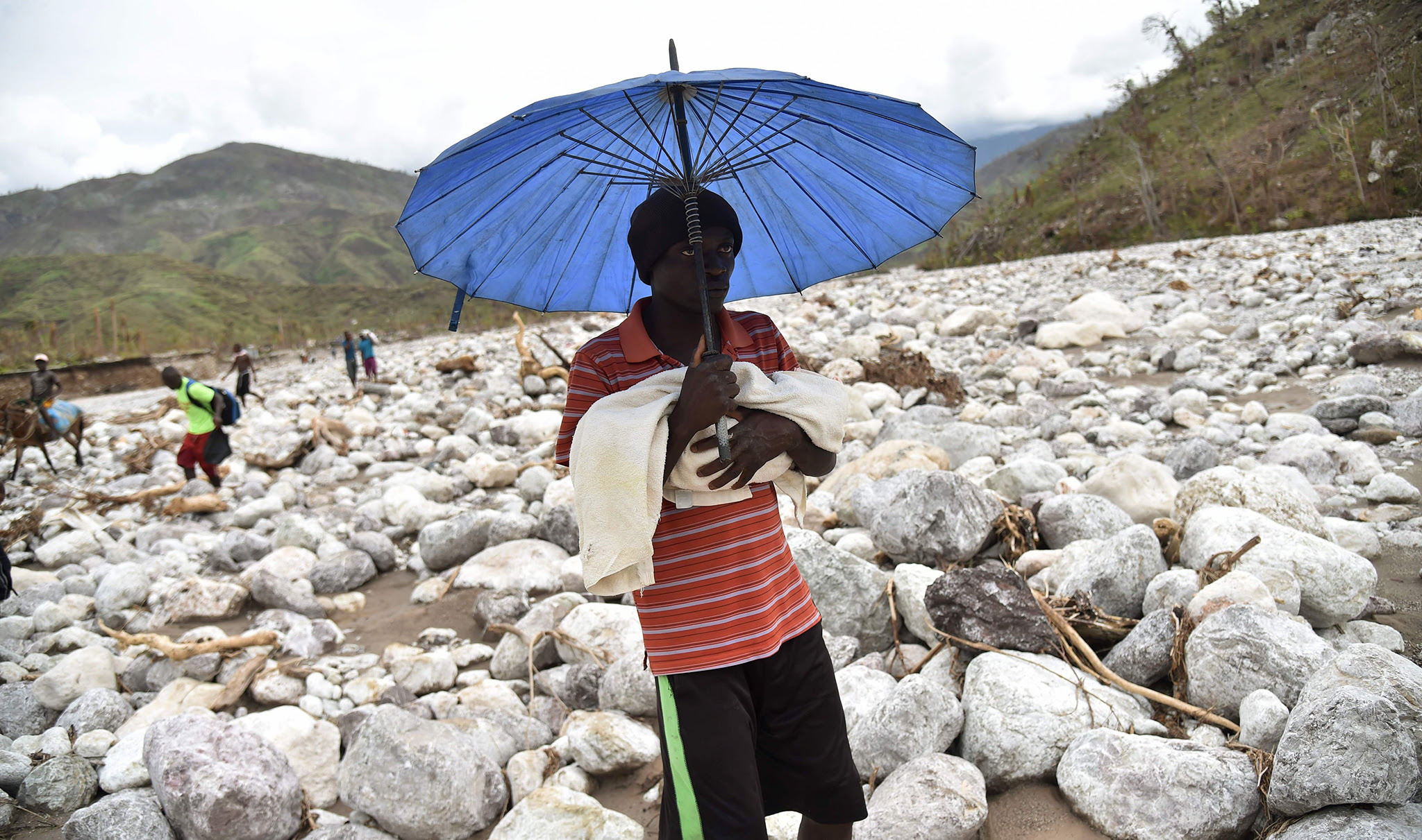 TOPSHOT - A man carries his baby on a trail in the middle of the river that passes near the village of Randelle, in the commune of Chardonniere, in the south west of Haiti, on October 19, 2016. The road leading to Randelle and other villages on the mountains was cut off after the passage of Hurricane Matthew. / AFP PHOTO / HECTOR RETAMALHECTOR RETAMAL/AFP/Getty Images