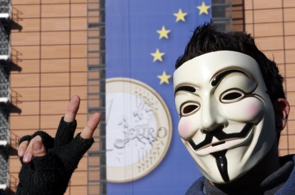 Un joven con una máscara de Anonymous frente a la Comisión Europea, en Bruselas (Bélgica), con la moneda de euro en su fachada. Foto: Reuters. Un joven con una máscara de Anonymous frente a la Comisión Europea, en Bruselas (Bélgica), con la moneda de euro en su fachada. Foto: Reuters.