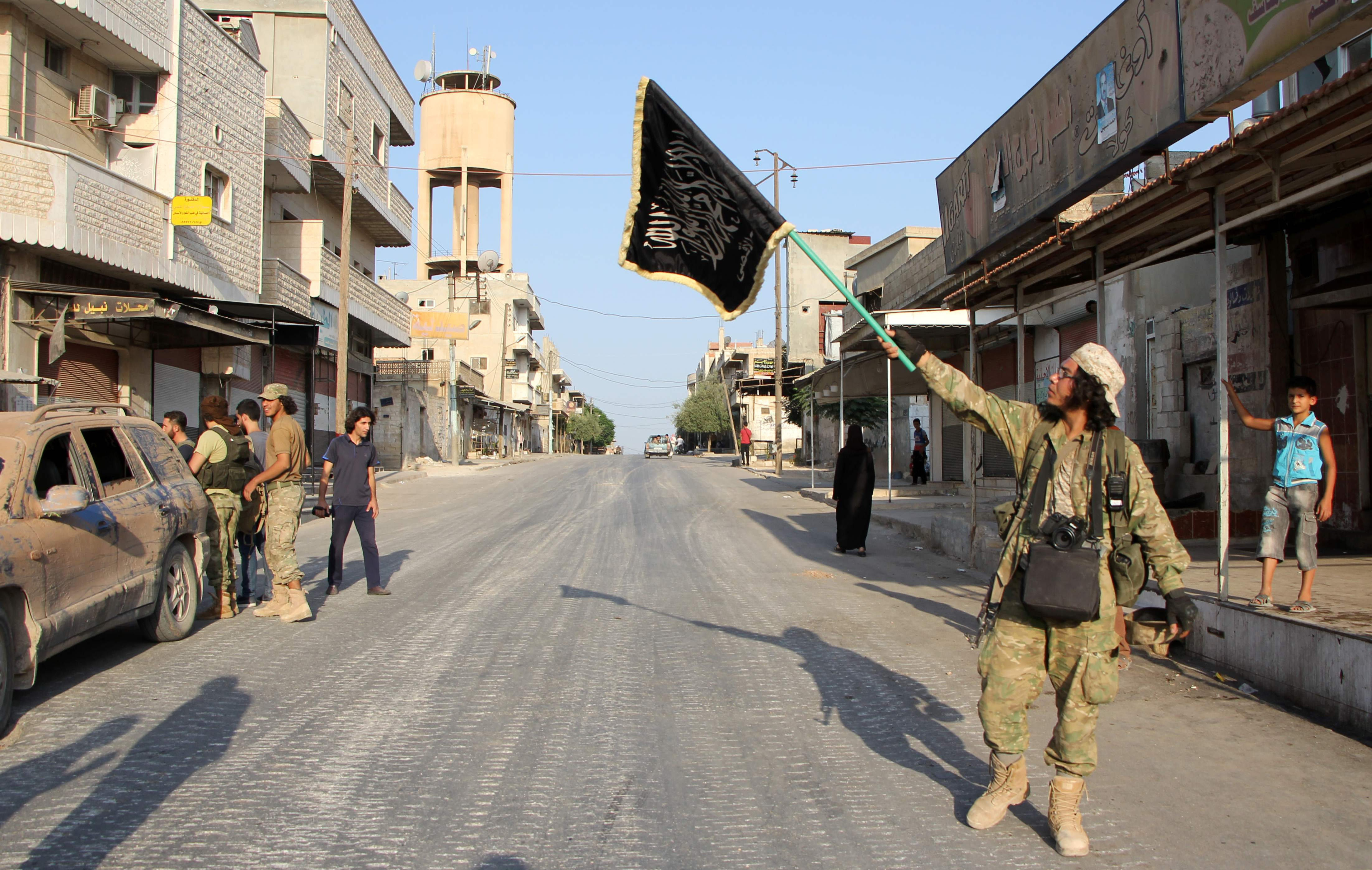 A fighter from the Jund al-Aqsa Islamist Brigade, raises an Islamist flag after taking control of the northern Syrian town of Tayyibat al-Imam, northwest of Hama from Syrian government forces
