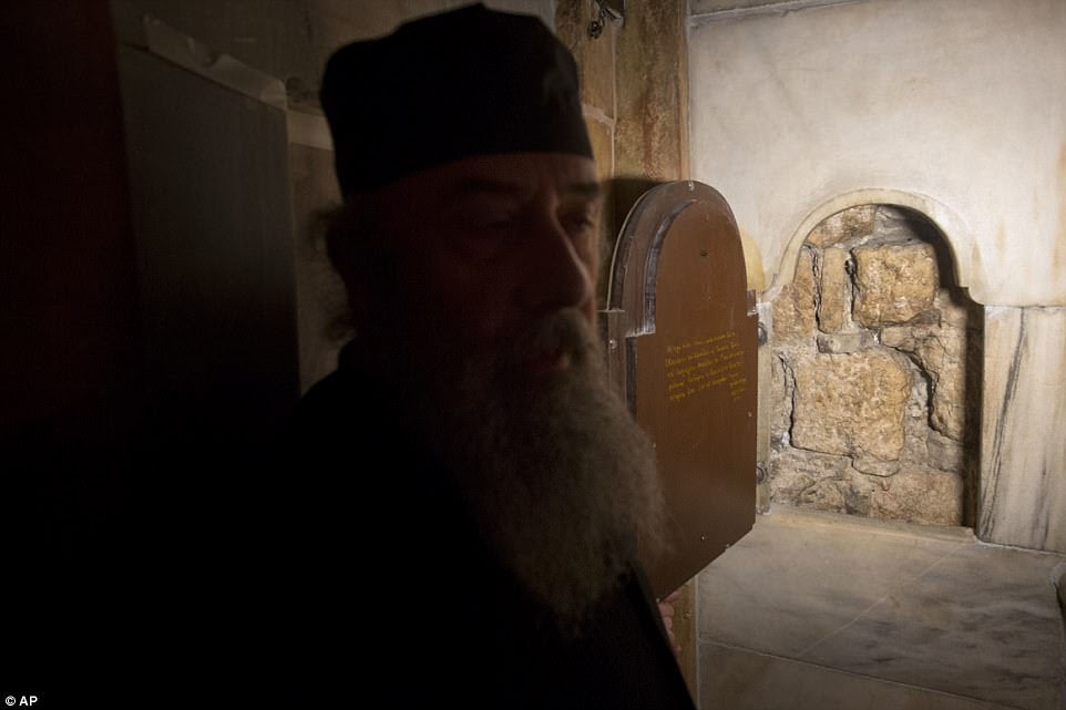 A Greek priest stands by a window into the burial chamber of Jesus' tomb for pilgrims to see what is believed to be the original stone wall of the burial cave inside the renovated Edicule in the Church of the Holy Sepulchre, traditionally believed to be the site of the crucifixion of Jesus Christ, in Jerusalem's old city Monday, Mar. 20, 2017. A Greek restoration team has completed a historic renovation of the Edicule, the shrine that tradition says houses the cave where Jesus was buried and rose to heaven.