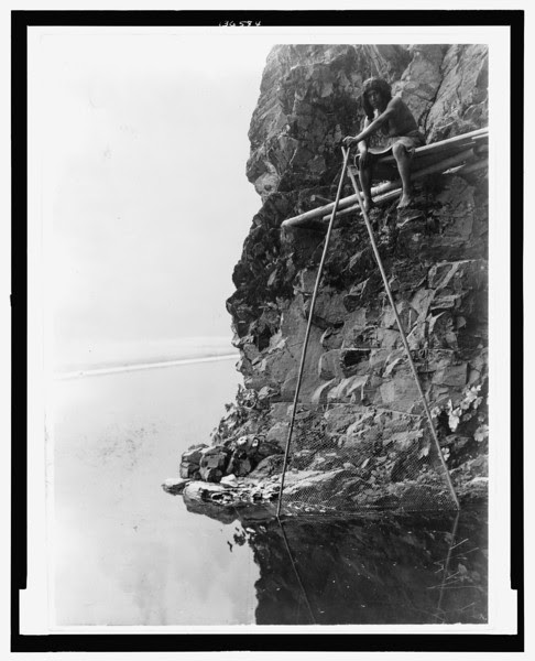 Description of  Title: Fishing platform on Trinity River--Hupa.  <br />Date Created/Published: c1923 Jun. 30.  <br />Summary: Photograph shows a Hupa man sitting on a platform on a rocky cliff, handling a fishing net.  <br />Photograph by Edward S. Curtis, Curtis (Edward S.) Collection, Library of Congress Prints and Photographs Division Washington, D.C.