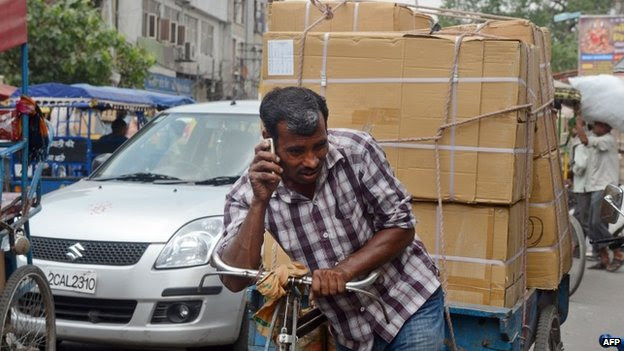 An Indian daily-wage labourer talks on his mobile phone as he transports goods on a rickshaw van down a busy street in New delhi on April 30, 2013