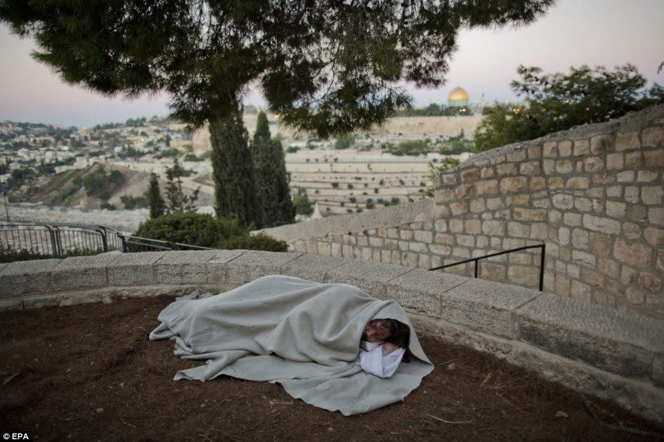 Copy cat: James Joseph has earned himself the nickname 'The Jesus Guy', and is living the life of the man the Bible calls 'The Son of God' in bare feet and robes, seen here as he sleeps near the ancient Jewish cemetery in Mount of Olives with the background of the Old City of Jerusalem