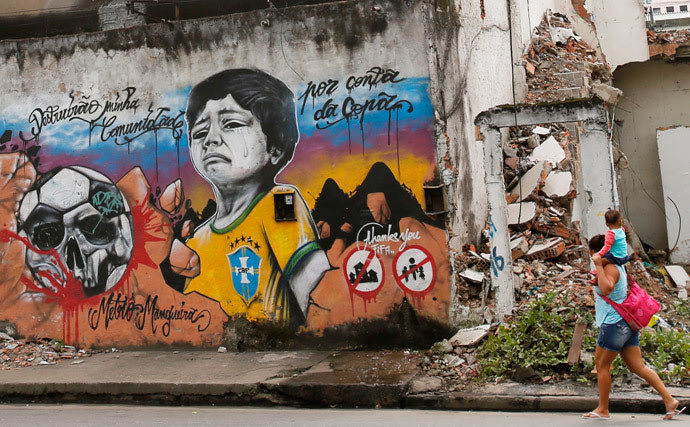 A woman walks with her child on her shoulders in front of graffiti against the infrastructure work for the 2014 World Cup at the Metro Mangueira slum near the Maracana Stadium in Rio de Janeiro April 10, 2013. (Reuters / Sergio Moraes)
