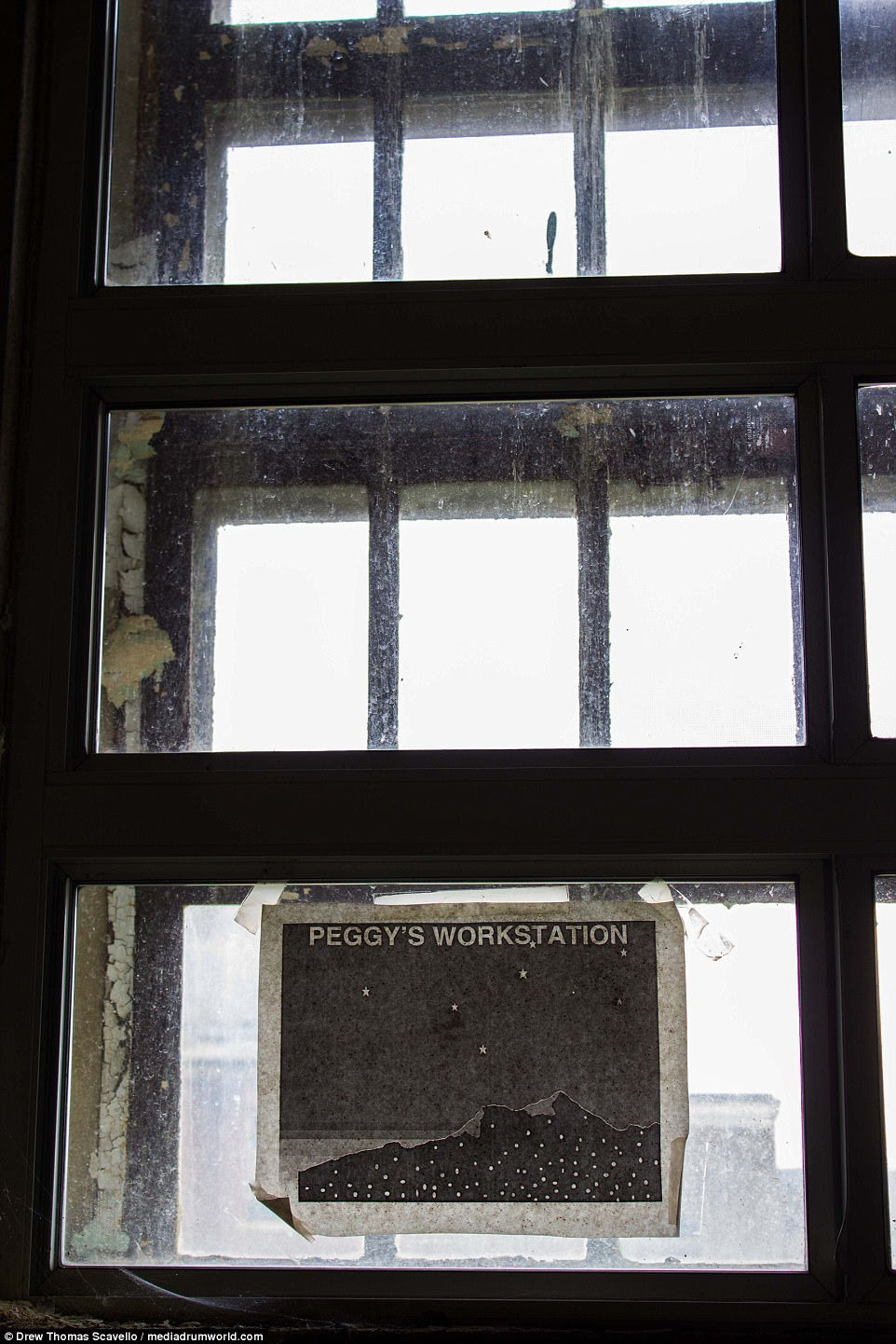 An old poster hangs in a filthy window at the former psychiatric asylum. It reads 'Peggy's Workstation' and shows a mountain at night with stars in the sky