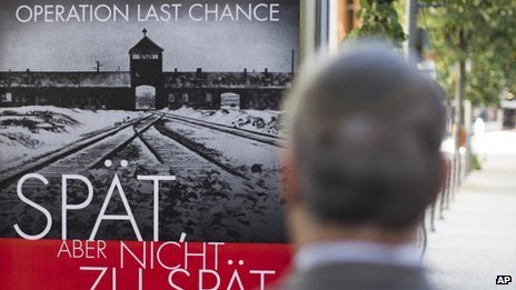 The Simon Wiesenthal Center's Efraim Zuroff stands in front of a poster reading "Operation last chance - late but not too late" on 23 July 2013