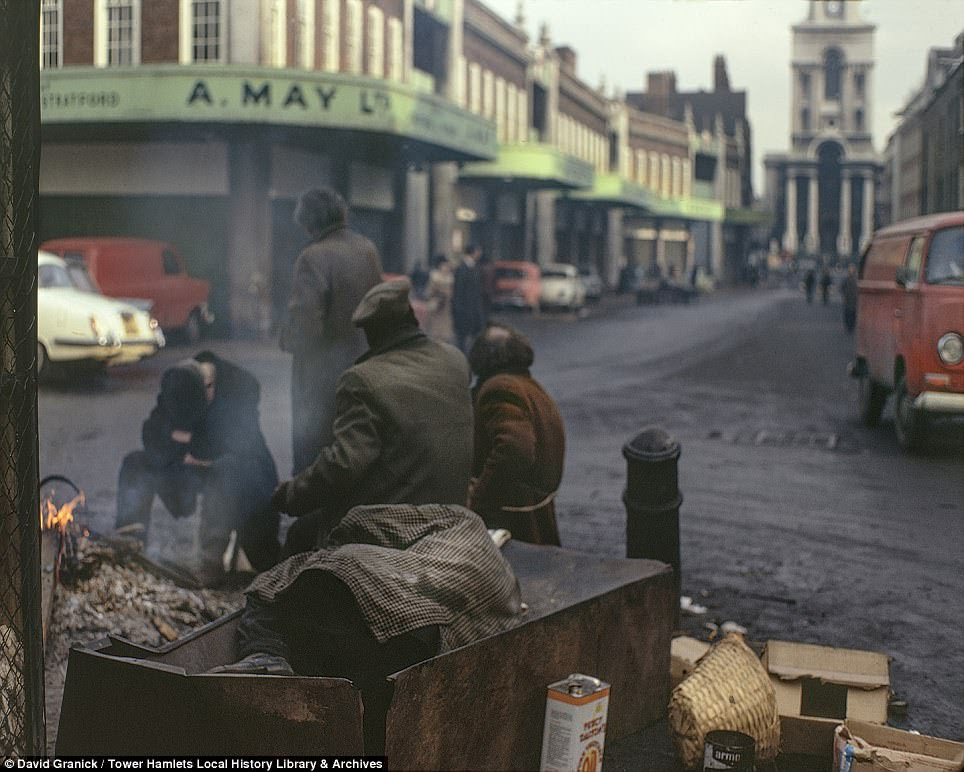 An intimate photograph from Spitalfields Market in 1973 shows men attempting to stay warm in the winter around a fire. The group has burnt several vegetable boxes and reveals the desperate poverty of the area experienced through the 20th century