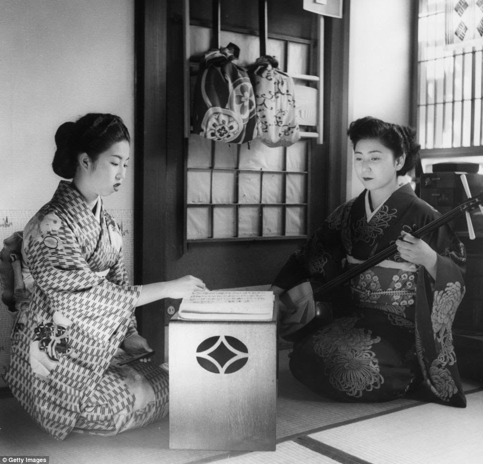 Two geisha girls practicing their art in the 1950s, one playing a samisen, a traditional Japanese stringed instrument