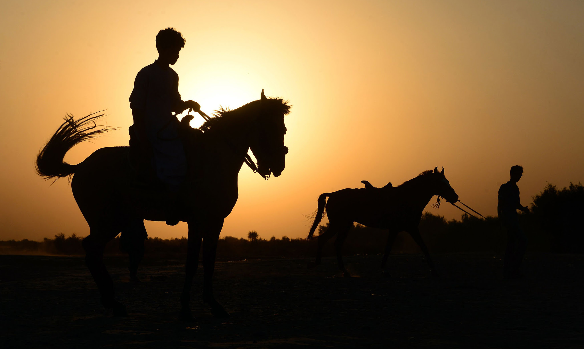TOPSHOT - In this photograph taken on July 28, 2016, an Afghan man rides a horse as another one leads his horse as the sun sets in Injil district of Herat province. / AFP PHOTO / AREF KARIMIAREF KARIMI/AFP/Getty Images