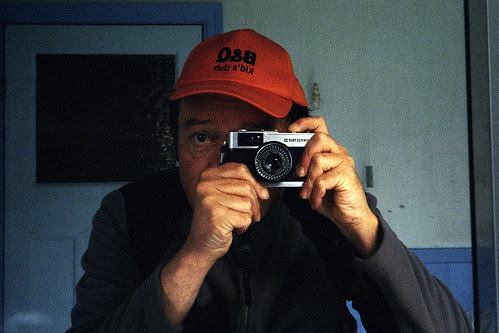 reflected self-portrait with Olympus Trip 35 camera and B&Q Kids Club cap by pho-Tony