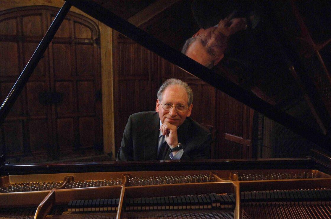 Dr. Orin Grossman sits at a piano smiling. 