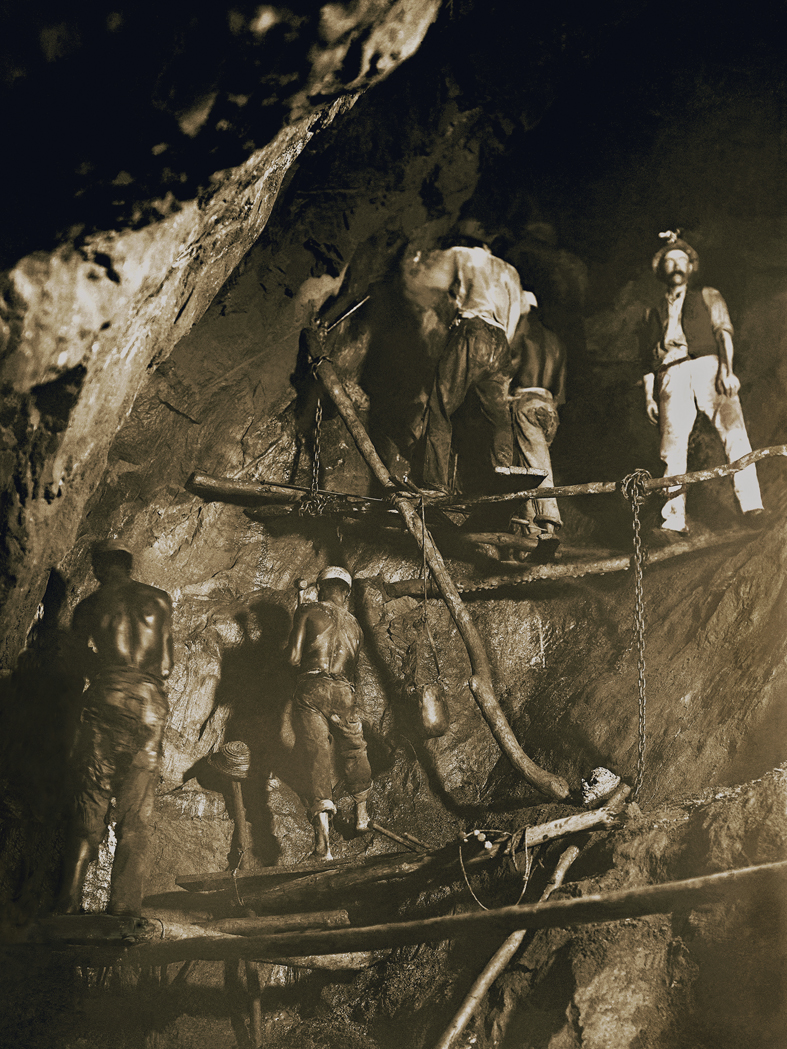 Quatro homens negros trabalhando em condições precárias, sobre todas de madeiras fixadas nas paredes de pedra, amarradas por cordas e grossas correntes. 