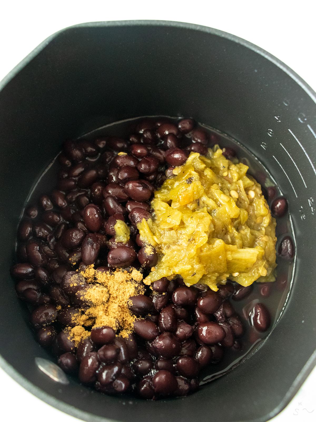 Black beans in a saucepan with fire roasted green chiles and ground cumin