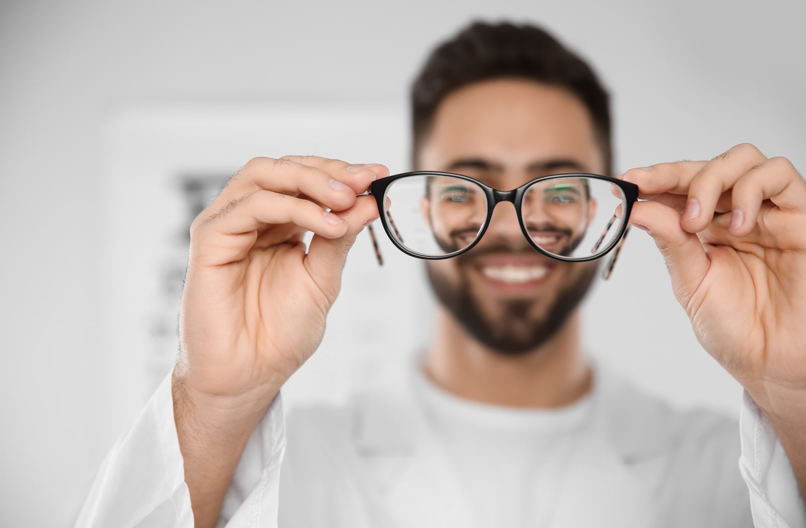 A man holding a pair of glasses in front of him, mimicking what myopia looks like.