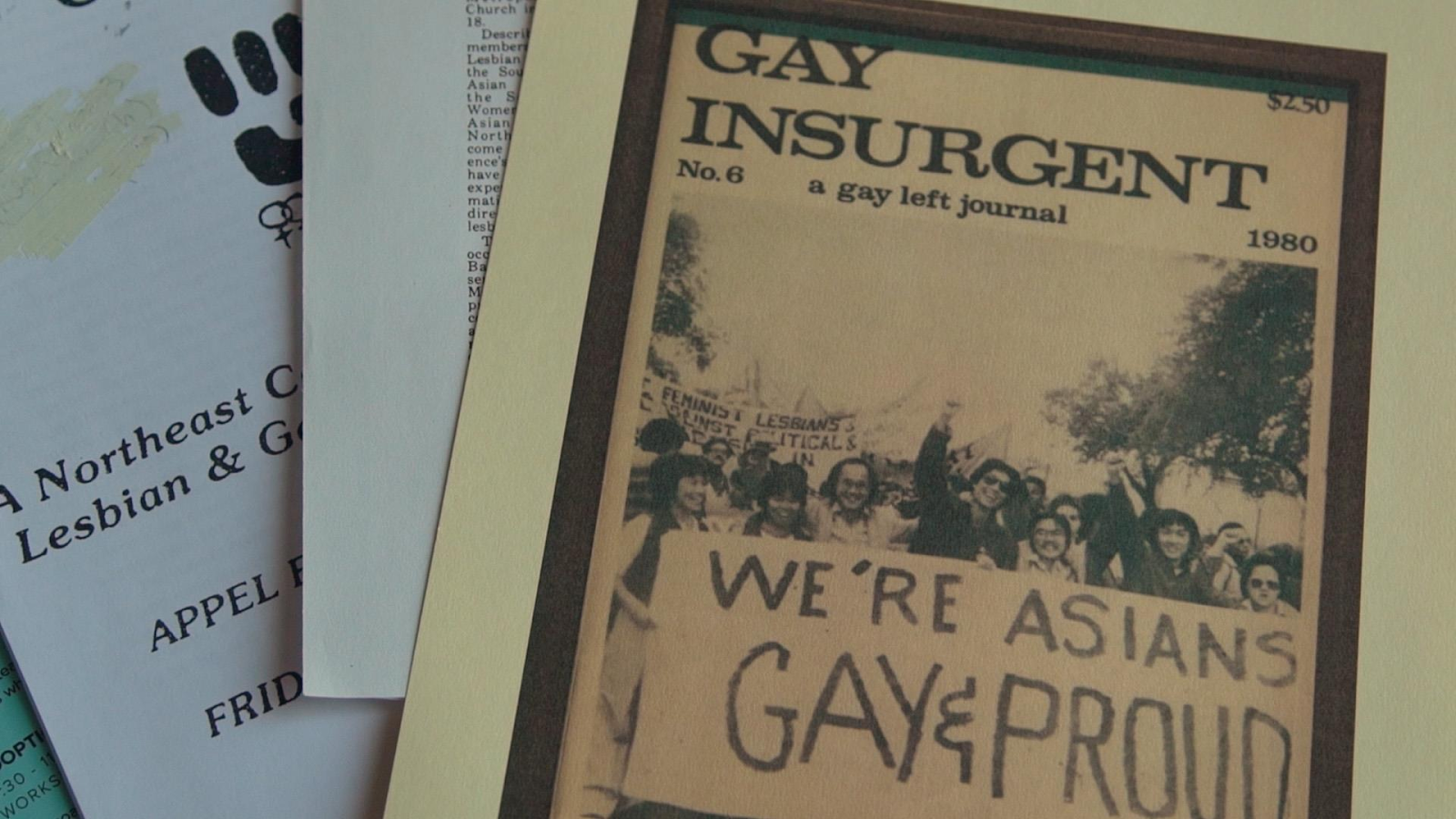 A stack of historical LGBTQ pamphlets and newsletters. On top is a copy of the gay left journal Insurgent with a photo of people marching with a banner that reads "We're Asians gay and proud" on the cover.