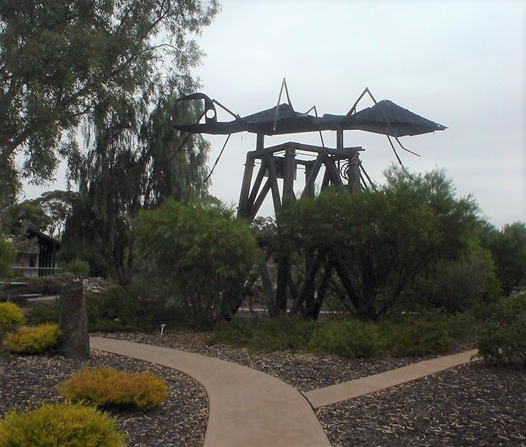 the big ant sculpture standing on a wooden structure surrounded by foliage in broken hill