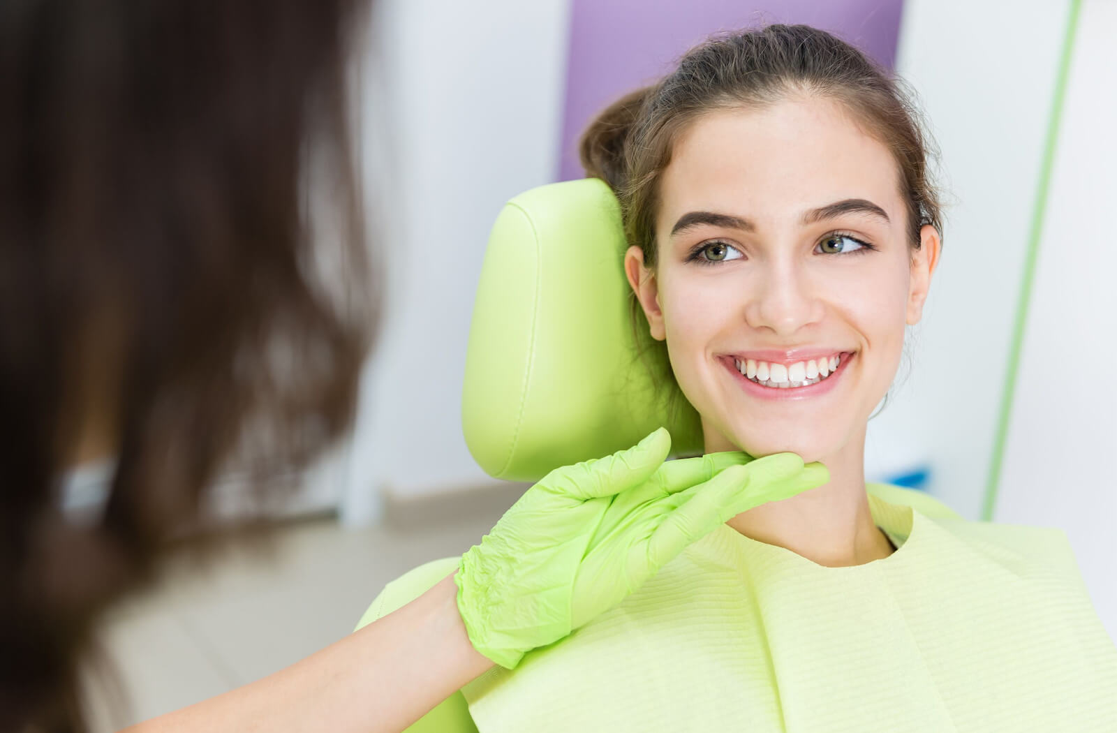 A woman sitting in a dentist's chair while a female dentist examines her teeth.