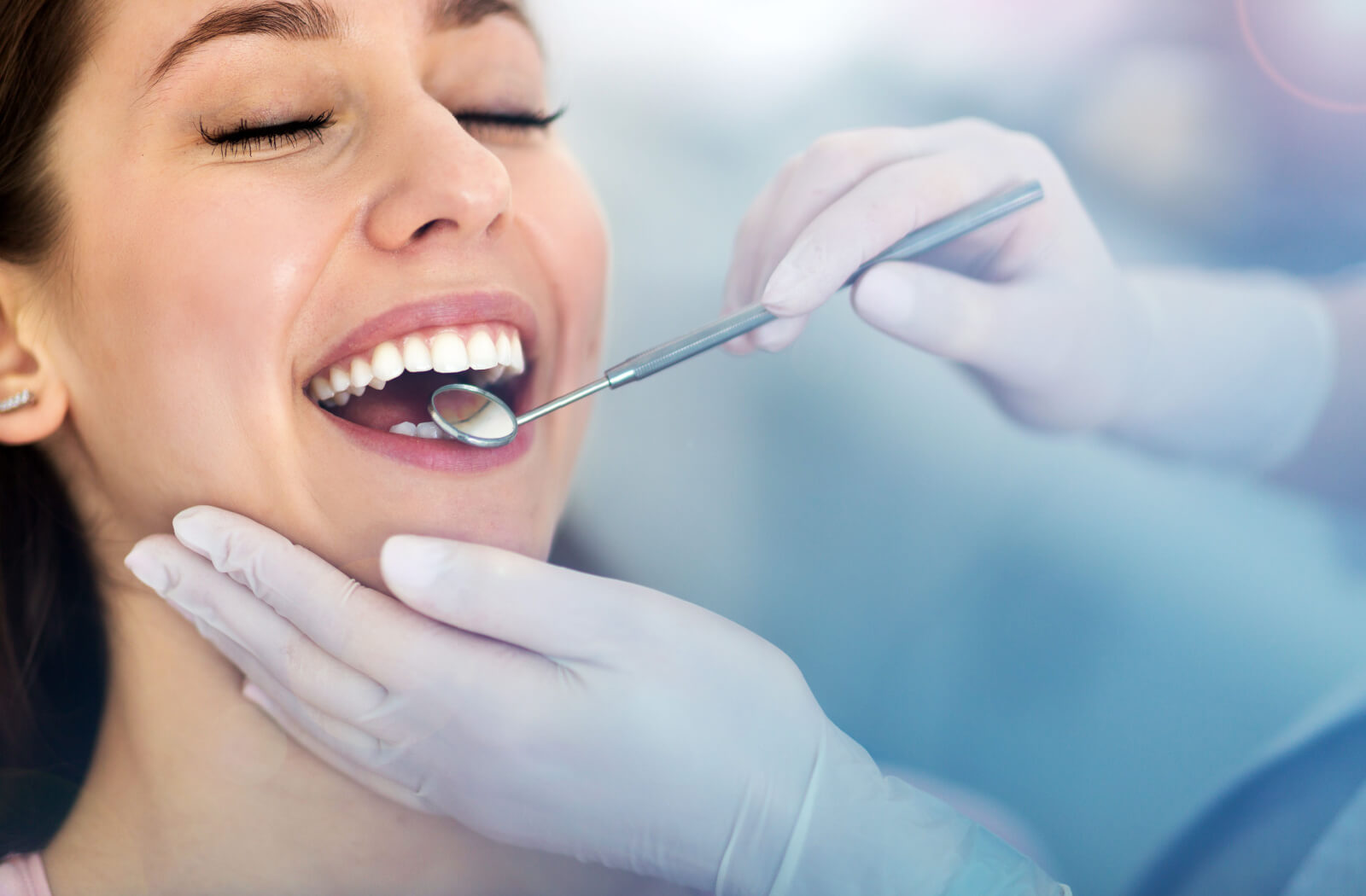 A close-up of a dentist's hands as they use a dental mirror to examine a woman's teeth.