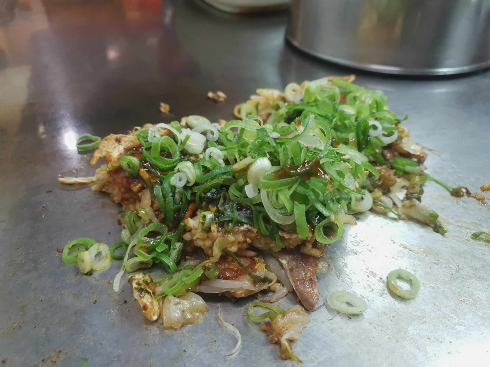 half eaten okonomiyaki with green onions on silver teppan