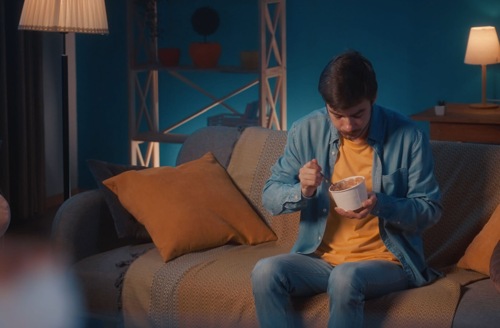 A a man recovering from a dental surgery eating ice cream while sitting on the sofa in the living room