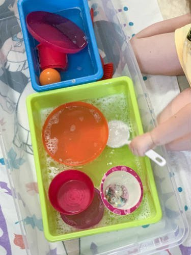 a child pretending to wash dishes in a plastic bin of soapy water