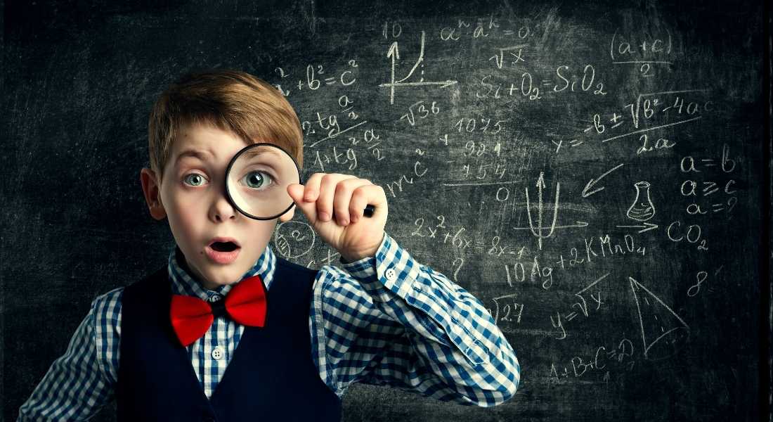 boy in front of chalkboard with math equations holding magnifying glass