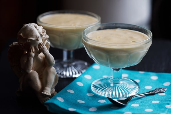 Vanilla pudding in a glass with a spoon on the side, placed on a white and blue polka dot cloth