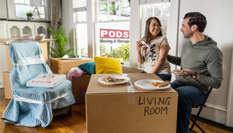 A couple eating pizza off of a moving box in their new Asheville home 