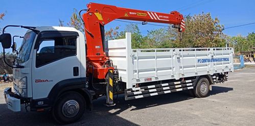 A truck mounted crane with white car paint, red crane set on the container. The mounted crane truck is parked on the road in front some trees