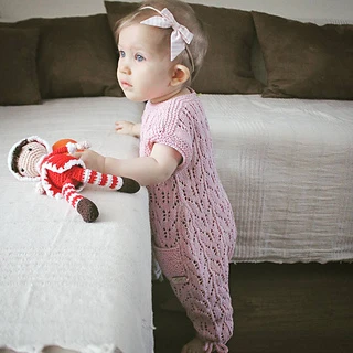 baby girl standing next to couch wearing a lacy pink romper