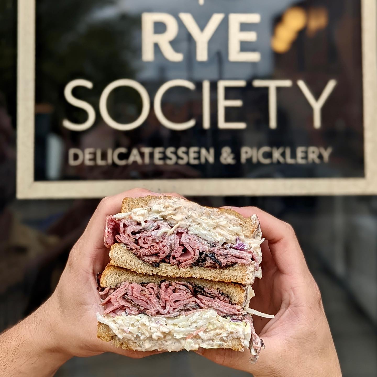 A person holding a Reuben sandwich outside Rye Society, a deli in Denver's RiNo neighborhood.