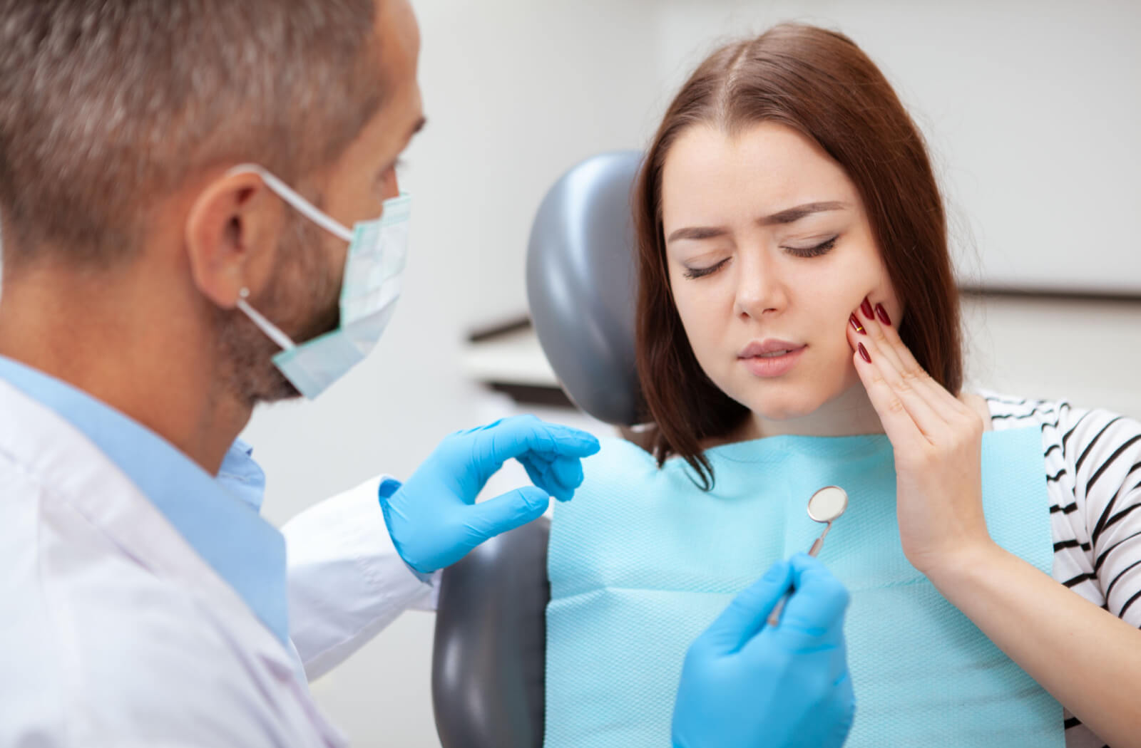 a woman in a dentists chair holds the side of her mouth due to a toothache from tooth decay