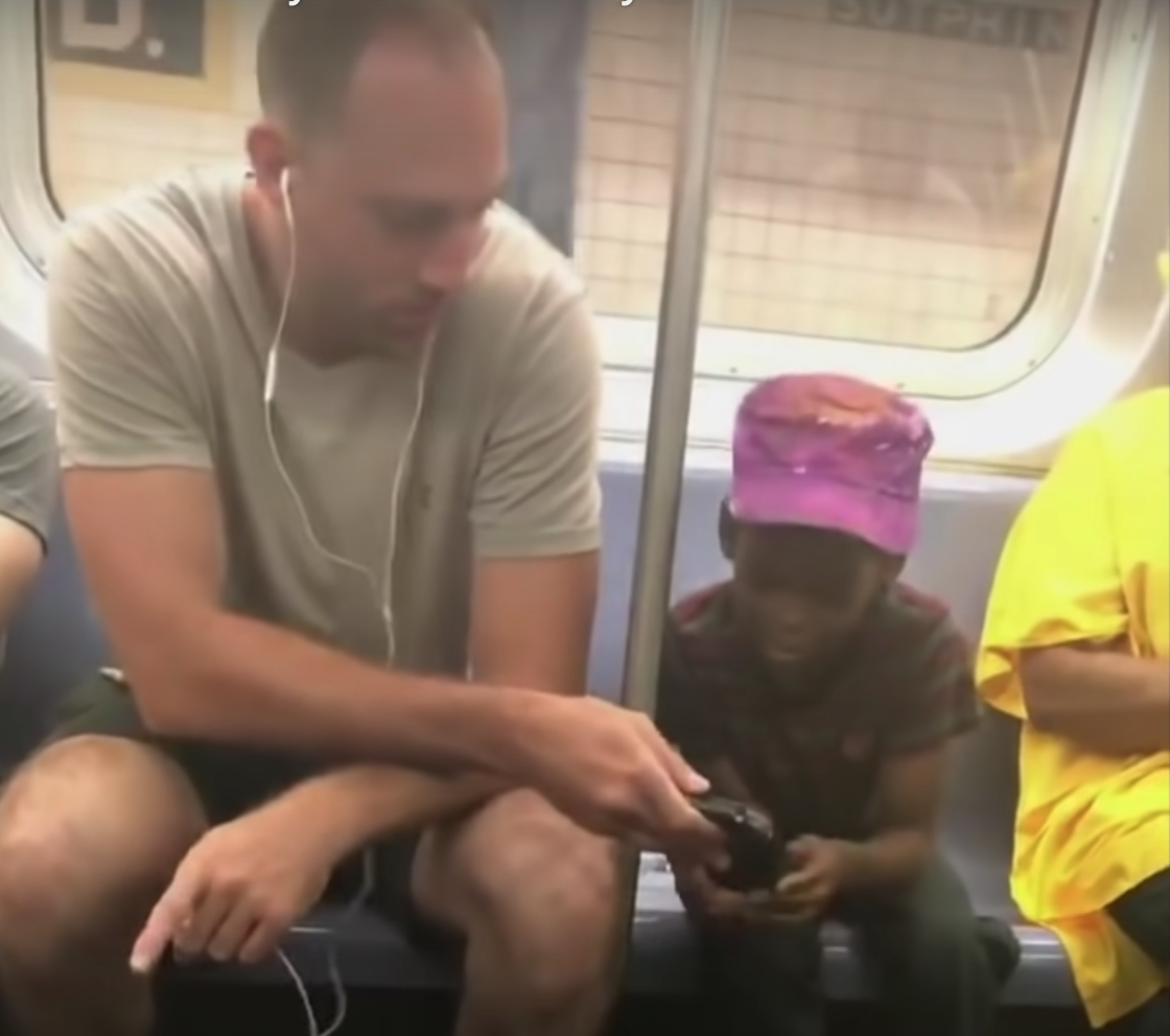 Man sharing phone with boy on the subway