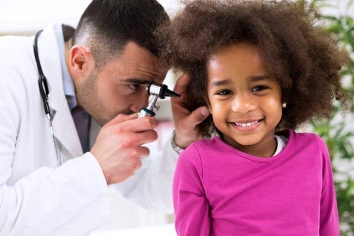 Un médecin ausculte l'oreille droite d'une enfant souriante 
