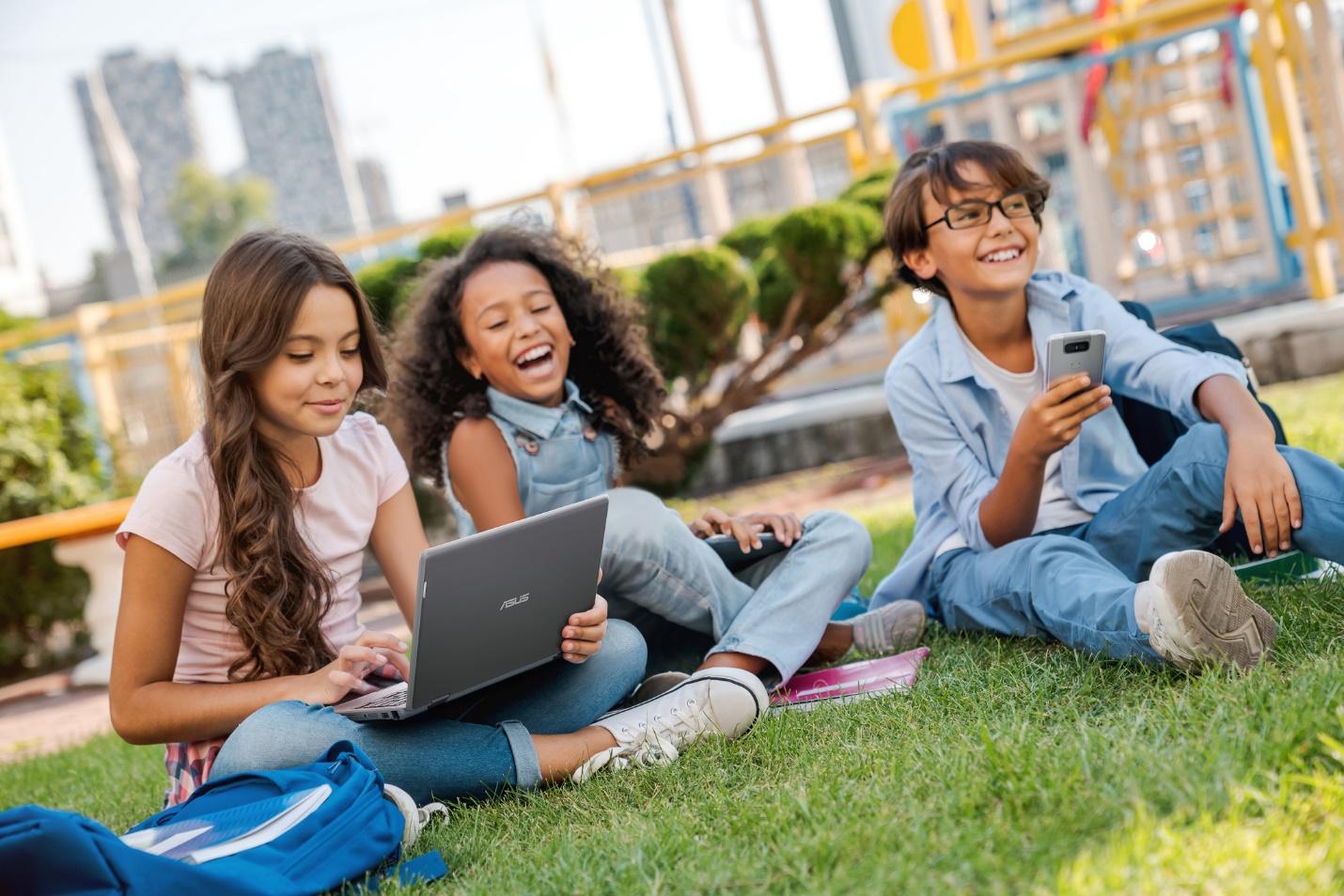 A group of girls sitting on the grass with a computerDescription automatically generated with low confidence