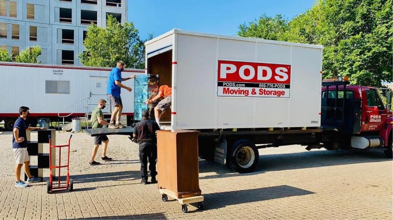 A group of men loading a PODS storage container on a parked truck.