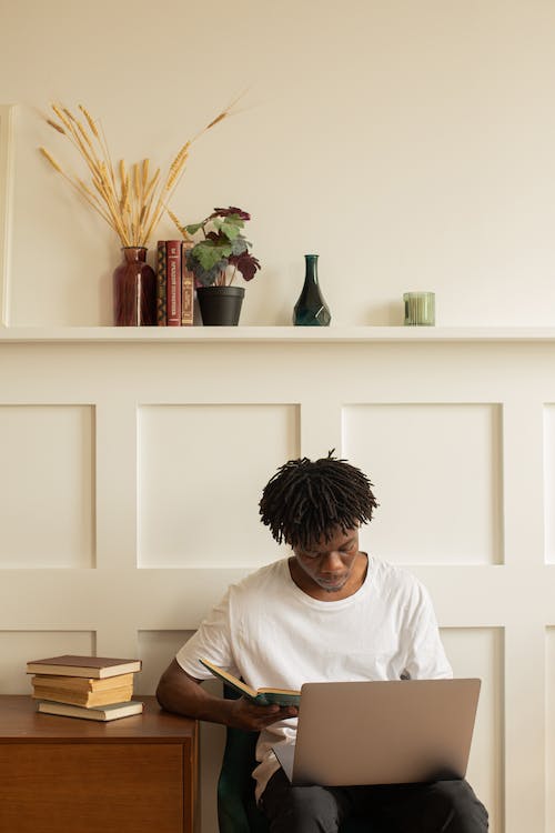 Free Man in White Shirt Sitting on Chair while Holding a Book and Laptop Stock Photo