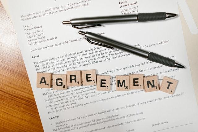 A lease agreement with two pens on top of it and a word agreement spelled with wooden blocks.