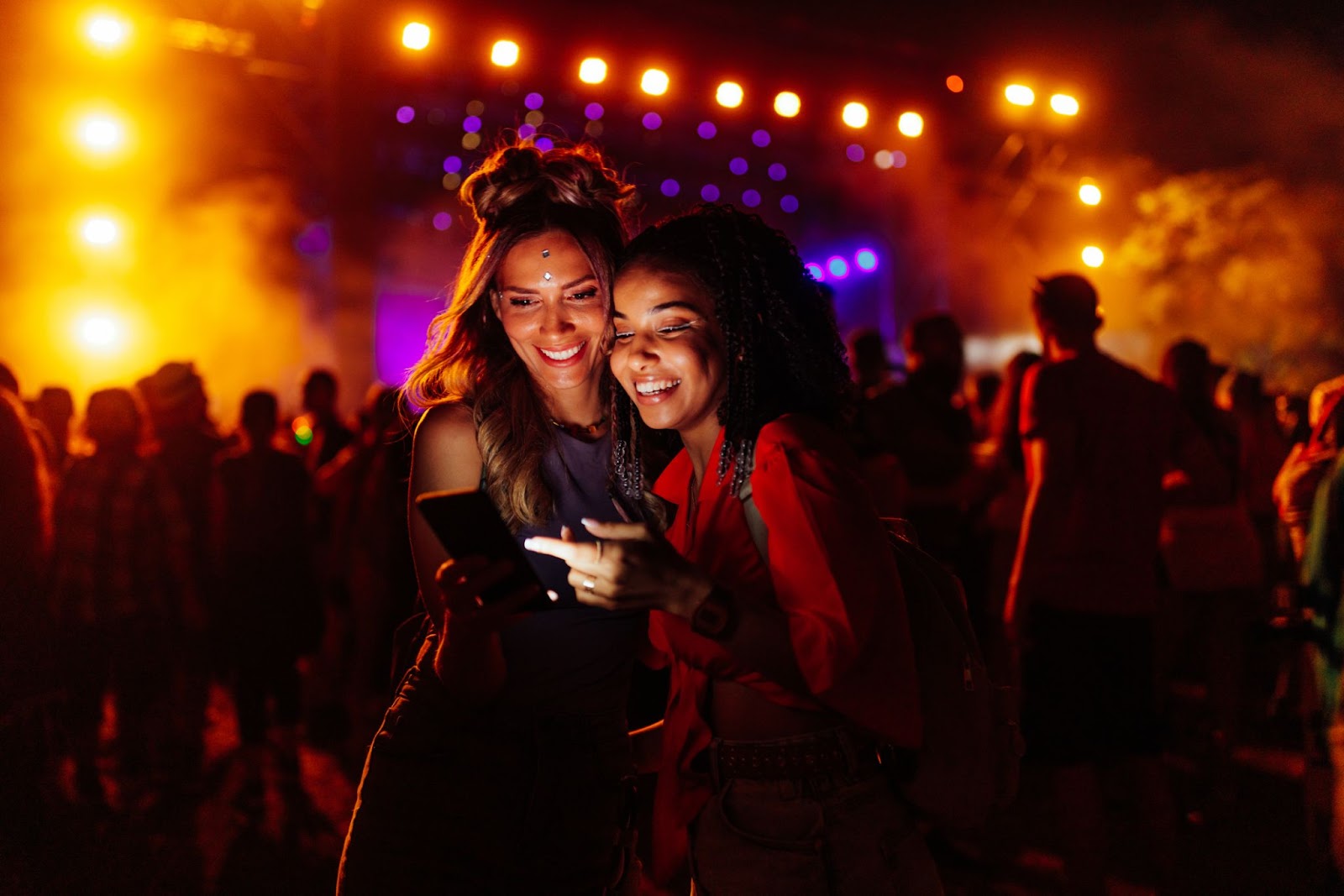 Two females at a Taylor Swift concert looking at a phone and smiling. 