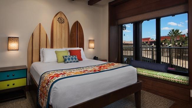 A bedroom featuring a bed, surfboard themed headboard and windows looking out toward the Resort area
